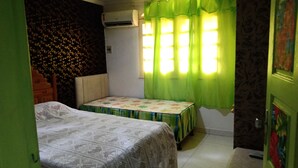 Una habitación pequeña con una cama, una mesita de noche, una ventana con cortinas verdes y un equipo de aire acondicionado en la pared.