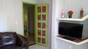 Una sala de estar con un sofá de cuero marrón, un televisor montado en una pared blanca y una puerta verde con paneles florales.