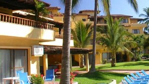 Un hotel con diversi balconi, palme e un prato curato.