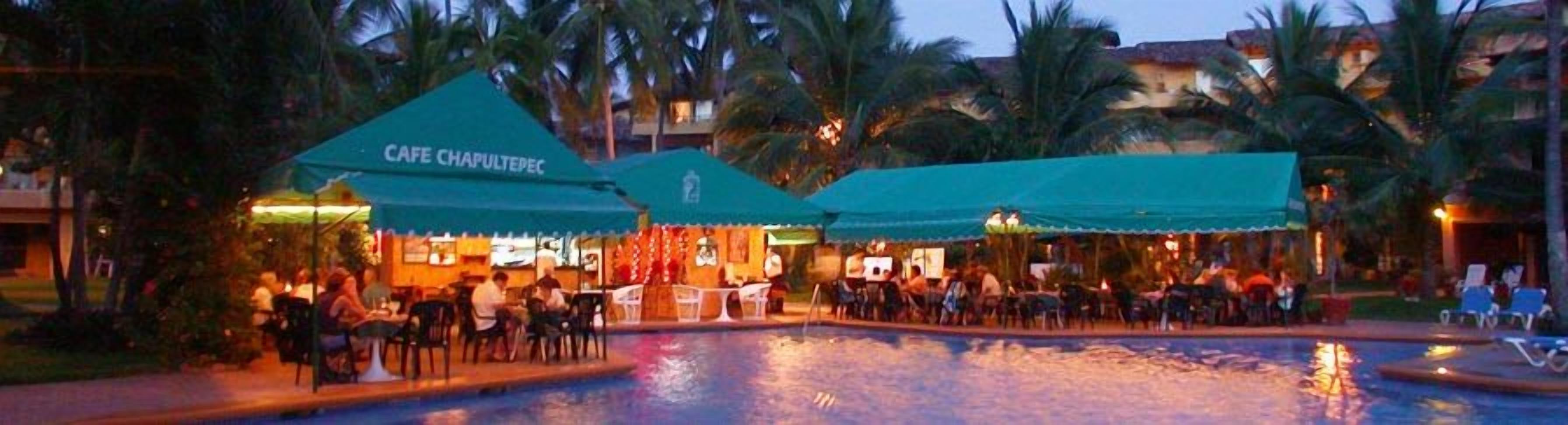 Un restaurant et un bar situés au bord de la piscine, avec des tables en plein air, des palmiers et une piscine.