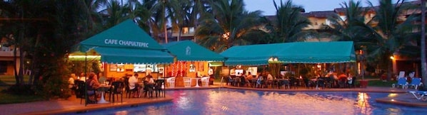 A poolside restaurant and bar with outdoor seating, palm trees, and a pool.