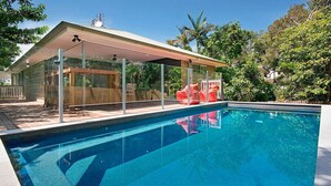Una piscina con un porche techado, rodeada de exuberante vegetación.