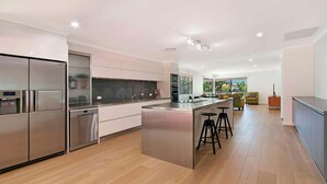 Una cocina moderna con electrodomésticos de acero inoxidable, una isla central con taburetes y vistas a una sala de estar con sofá y mesa de comedor.