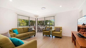 Amplia sala de estar con un sofá grande, dos sillones y una mesa de centro. Cuenta con un balcón con una mesa y sillas, y un televisor montado en la pared.