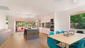Una cocina moderna con una isla central, un comedor con sillas azules y vistas a zonas verdes.