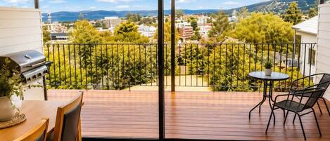 Un balcón con vistas a un paisaje urbano, una parrilla y una mesa con sillas.