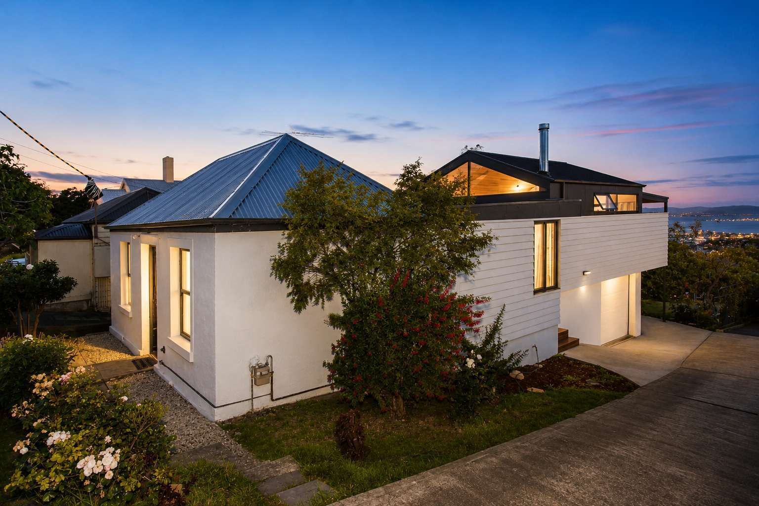 A modern two-story house with a sloped roof, a visible chimney, and a well-maintained garden.