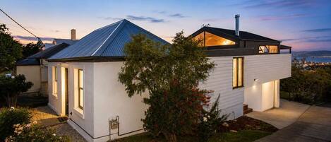 A modern two-story house with a sloped roof, a visible chimney, and a well-maintained garden.