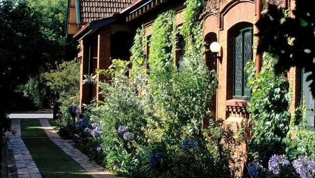 Ein traditionelles Haus mit Backsteinfassade, Ziegeldach und einem Garten mit verschiedenen Pflanzen und Blumen.