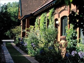 Et traditionelt hus med murstensfacade, tegltag og en have med forskellige planter og blomster.