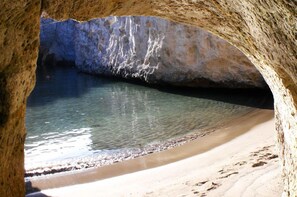 A natural cave formation with a sandy beach and clear water.