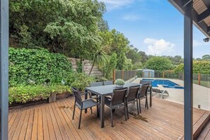 Eine Terrasse im Freien mit Tisch und Stühlen, umgeben von üppiger Vegetation und einem Schwimmbad.