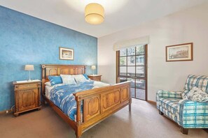 A bedroom with a wooden bed, a nightstand, a chair, and a window with a view.