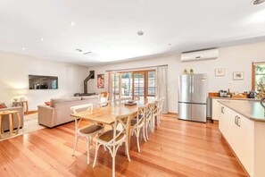 A modern kitchen with a dining area, wooden flooring, and a built-in refrigerator.