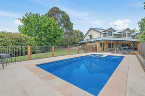 A rectangular swimming pool with a clear blue surface, surrounded by a paved deck.
