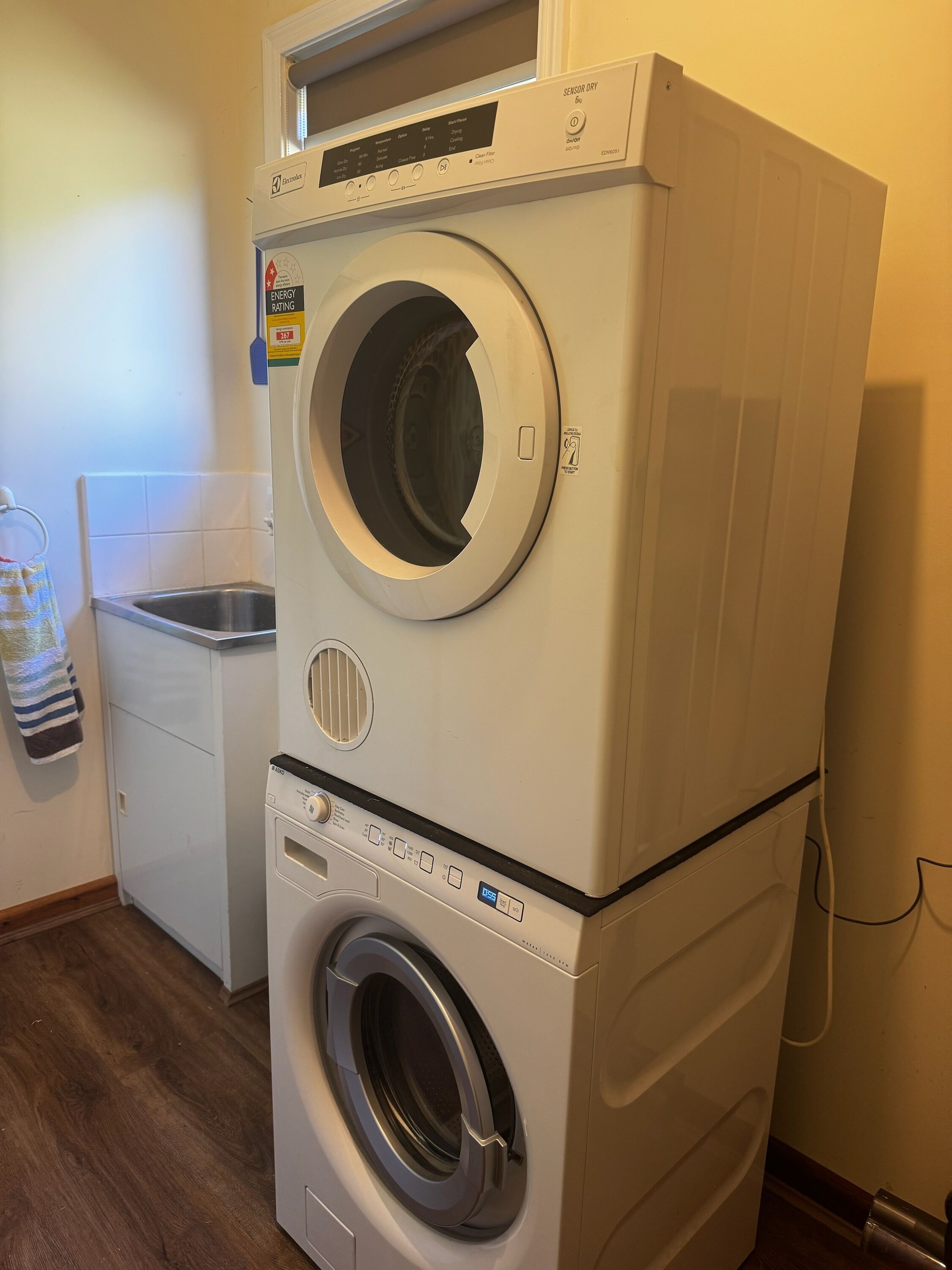 Una lavadora y secadora apiladas en un cuarto de lavado, con un lavamanos pequeño y un perchero.