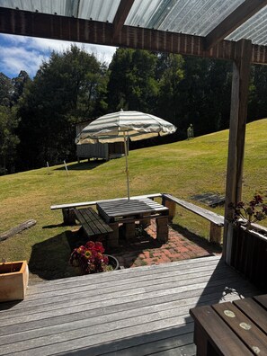 Een overdekt terras met een tafel, stoelen, een gestreepte parasol en een houten terras.