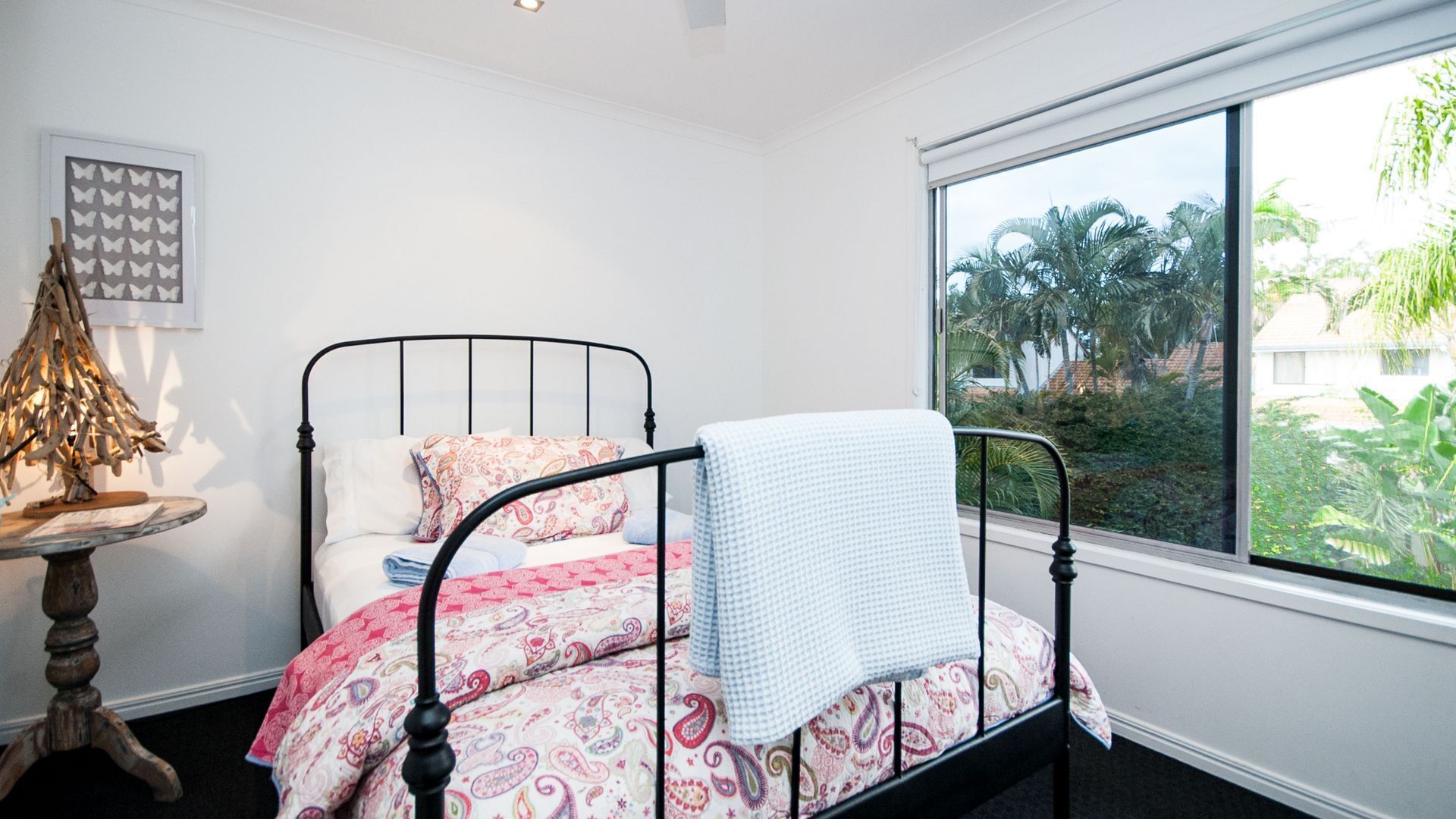 Un dormitorio con una cama, una ventana con vistas a palmeras y una obra de arte en la pared.