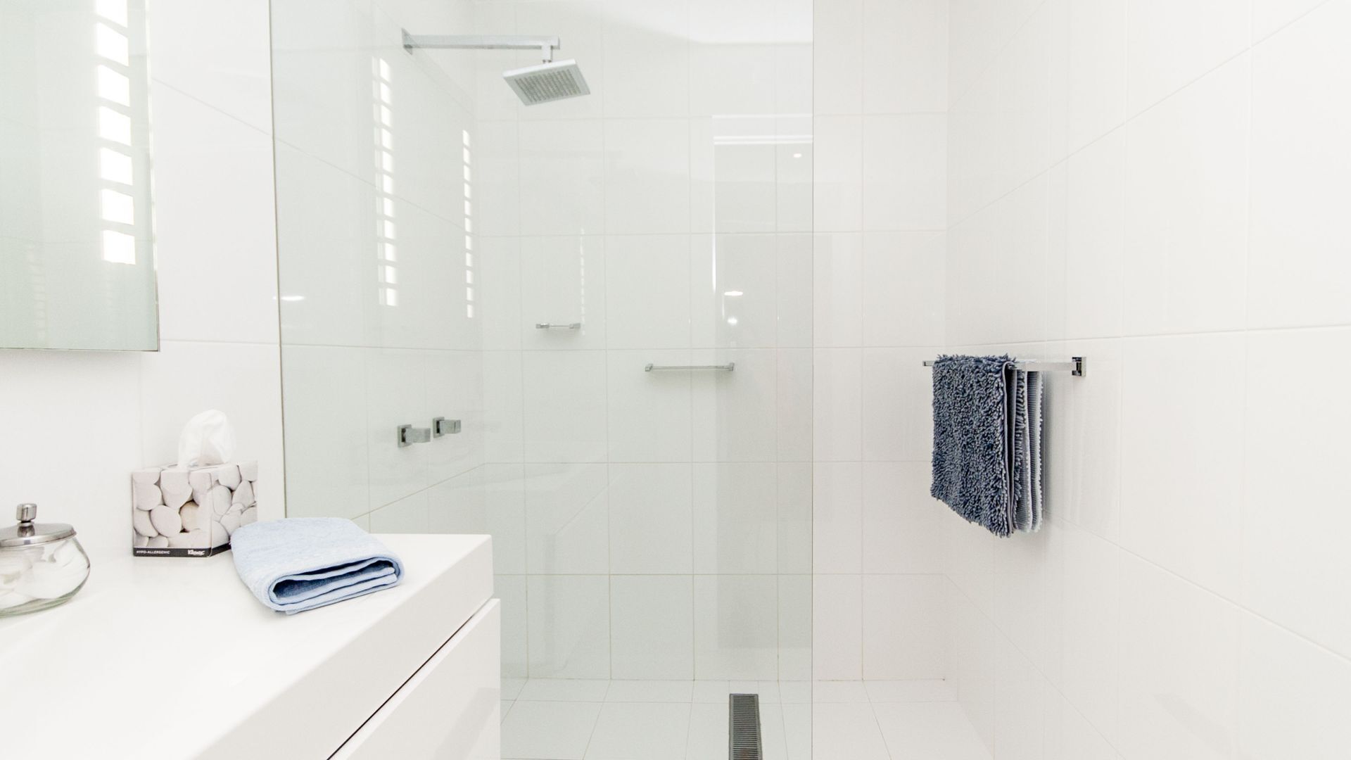 A modern bathroom with a glass shower enclosure, a white vanity with a towel, and a towel rack with a patterned towel.