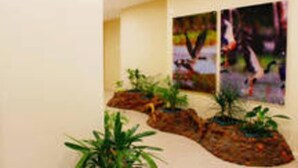 A hallway with two paintings on the wall, a plant arrangement, and a textured wall. - Nomiki across the avenue (parap)