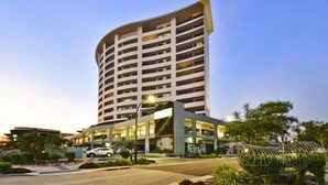 A modern hotel with a curved facade, multiple balconies, and a landscaped entrance area. - Nomiki across the avenue (parap)