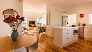 A modern kitchen with a central island, white cabinetry, and a dining area with a wooden table and chairs. - Oneroa Village, 5 mins to Oneroa beach, Restaurants & Shops | Be My Guest (Oneroa)