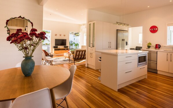 A modern kitchen with a central island, white cabinetry, and a dining area with a wooden table and chairs.