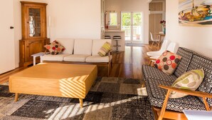 A living room with a sofa, ottoman, and patterned armchair, a wooden cabinet, and a painting on the wall. - Oneroa Village, 5 mins to Oneroa beach, Restaurants & Shops | Be My Guest (Oneroa)