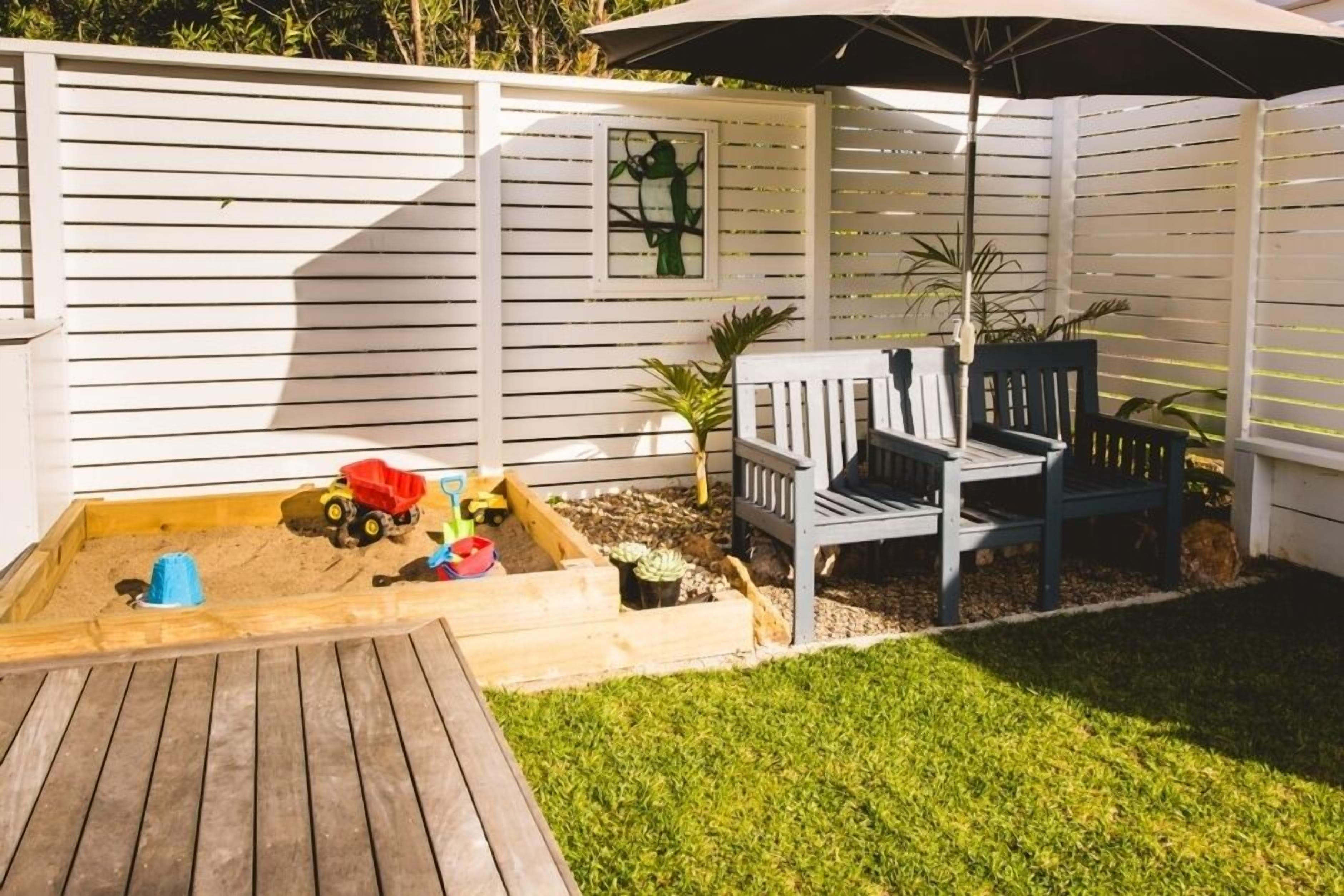 A wooden deck with a sandbox, two chairs, and a small table.