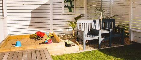 A wooden deck with a sandbox, two chairs, and a small table.
