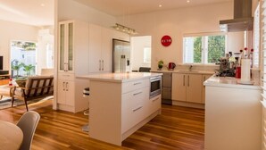 A modern kitchen with white cabinetry, a central island, and a dining area with a wooden floor. - Oneroa Village, 5 mins to Oneroa beach, Restaurants & Shops | Be My Guest (Oneroa)