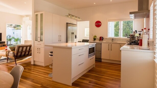 Une cuisine moderne avec des meubles blancs, un îlot central et un coin repas doté d’un plancher en bois.
