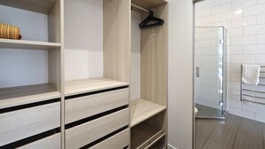 A modern bathroom with a glass shower enclosure, white tiled walls, and a wooden vanity with open shelves. - Oneroa Village, 5 mins to Oneroa beach, Restaurants & Shops | Be My Guest (Oneroa)