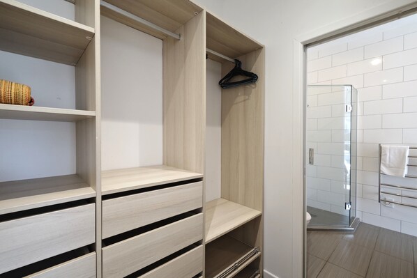 A modern bathroom with a glass shower enclosure, white tiled walls, and a wooden vanity with open shelves. - Oneroa Village, 5 mins to Oneroa beach, Restaurants & Shops | Be My Guest (Oneroa)