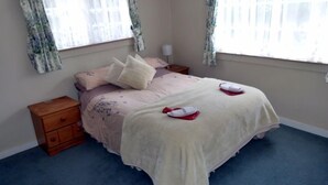 Une chambre à coucher comprenant un lit, deux tables de chevet, une commode en bois et une fenêtre agrémentée de rideaux à motifs floraux.