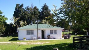 Un petit bâtiment blanc avec un toit vert, une véranda avec des chaises et une clôture en bois au premier plan.