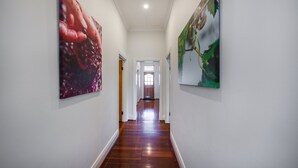 Un couloir doté d’un plancher en bois, de murs blancs et de deux grandes peintures de chaque côté.