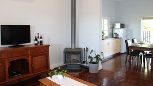 Un salon comprenant un téléviseur, un meuble en bois, une cheminée, un coin repas avec des chaises et une cuisine équipée.