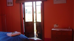A room with a bed, a dresser, and a door leading outside. - Quaint character cottage on working farmlet, Running Sheep & Beef. (Upper Moutere)