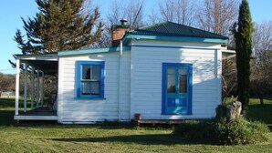 A small, single-story house with a porch and a chimney. - Quaint character cottage on working farmlet, Running Sheep & Beef. (Upper Moutere)