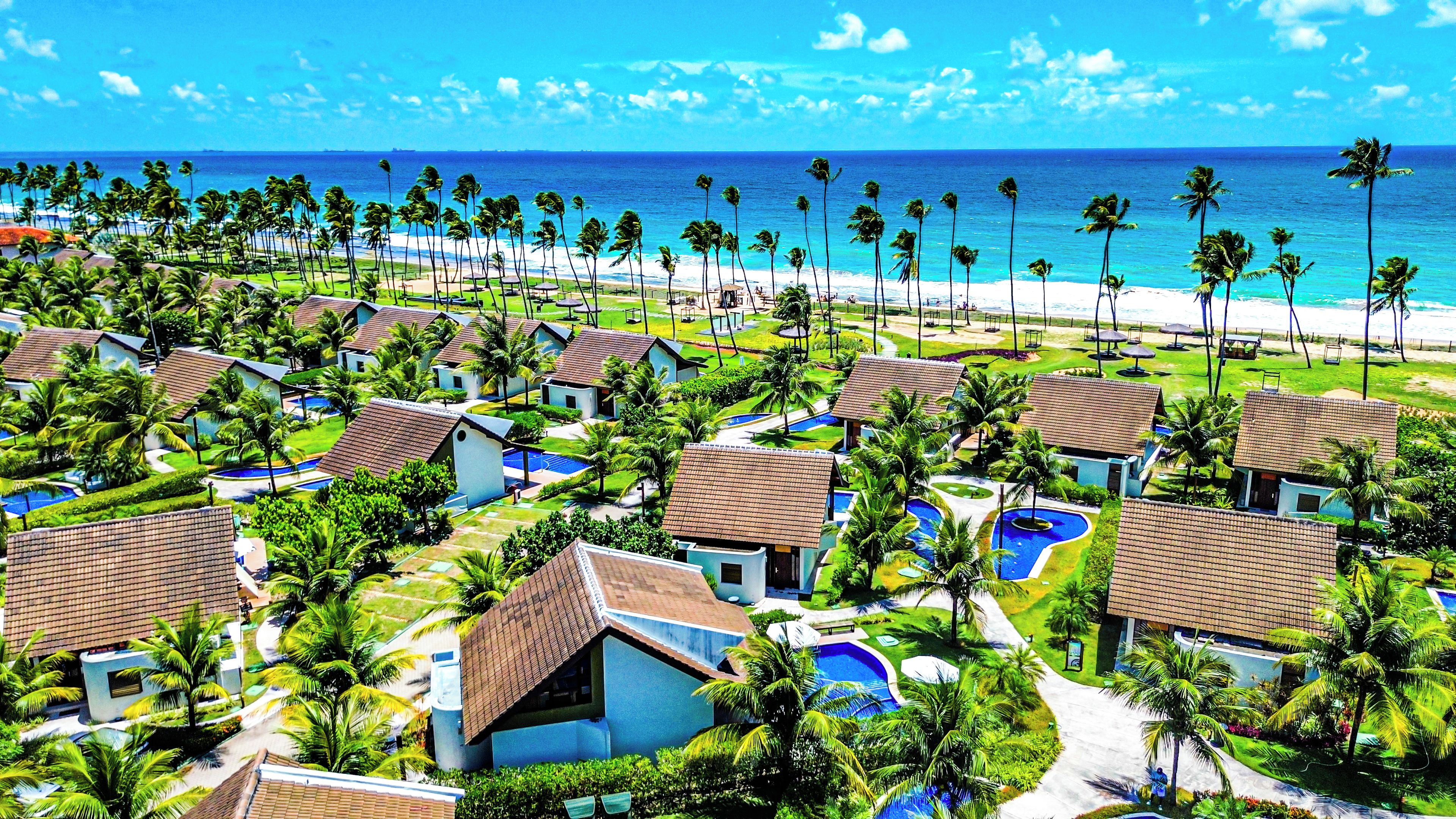 A resort with multiple bungalow-style buildings, a central pool area, and a beach view.