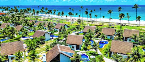 A resort with multiple bungalow-style buildings, a central pool area, and a beach view.
