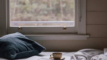 A bed with a cup of coffee, a pillow, and a window with a view of trees.