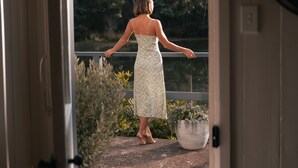 A woman in a floral dress standing at a doorway with a view of a forest and a railing. - Naivasha Cottage with antique outdoor bath (REEDY MARSH)