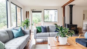 A modern living room with a grey sofa, a wooden coffee table, and a black wood-burning stove. - Naivasha Cottage with antique outdoor bath (REEDY MARSH)