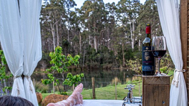 A person relaxing in a hot tub with a bottle of wine and a glass on a wooden stand. - Naivasha Cottage with antique outdoor bath (REEDY MARSH)