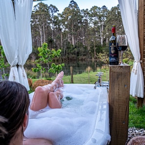 A person relaxing in a hot tub with a bottle of wine and a glass on a wooden post. - Naivasha Cottage with antique outdoor bath (REEDY MARSH)