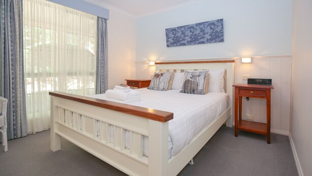 A bedroom with a bed, bedside tables, a nightstand, a window with curtains, and a wall-mounted artwork. - AMBER COTTAGE: Bright (Bright)