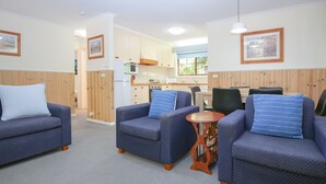 A cozy room with two blue armchairs, a small wooden table, and a kitchenette in the background. - AMBER COTTAGE: Bright (Bright)