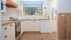 A compact kitchen with a built-in oven, a dishwasher, and a window with a view of greenery. - AMBER COTTAGE: Bright (Bright)